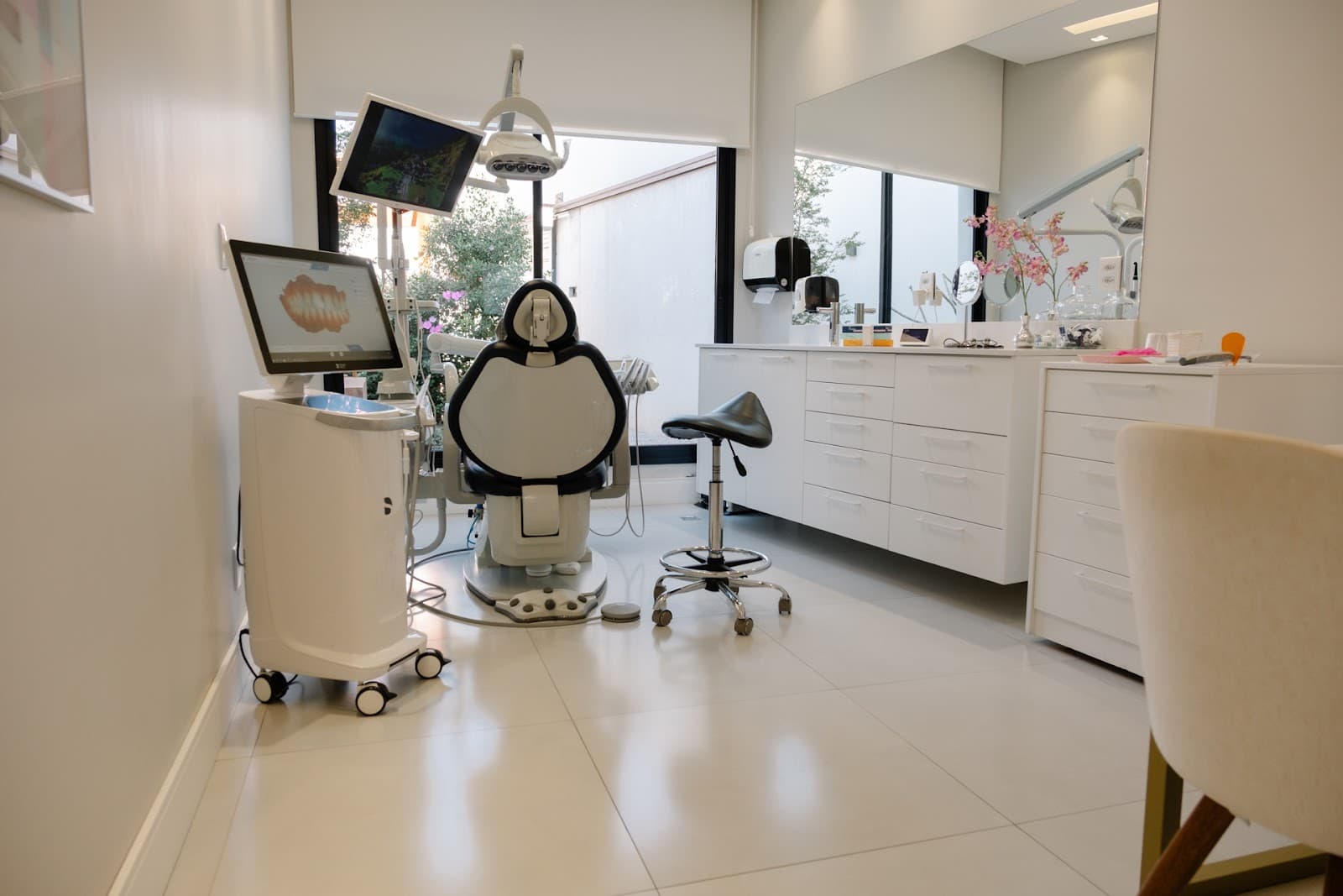 Consultório com cadeira odontológica, escâner intraoral com a arcada na tela e janela para o jardim