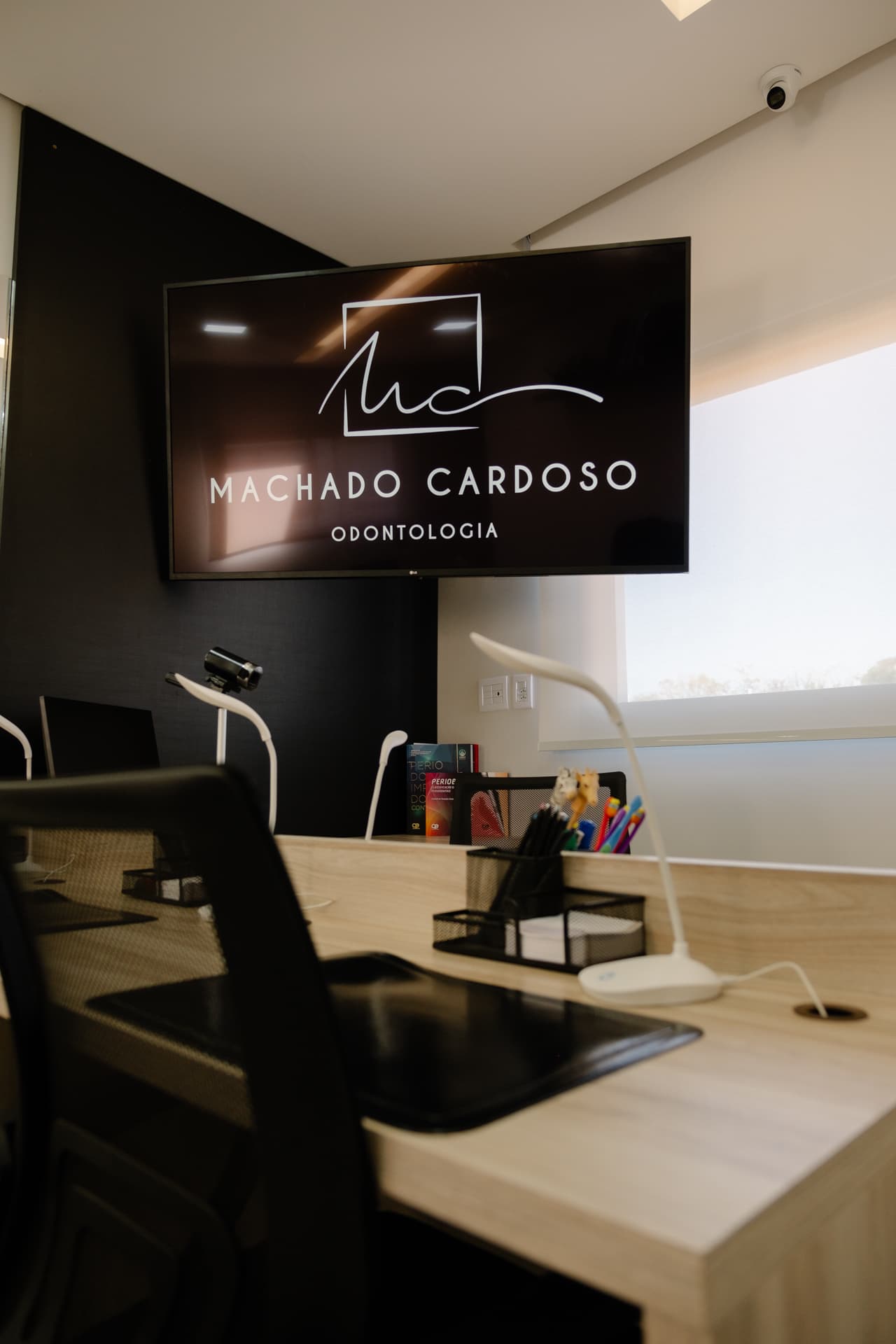 Sala de planejamento com mesa de madeira e a TV com o logo Machado Cardoso Odontologia