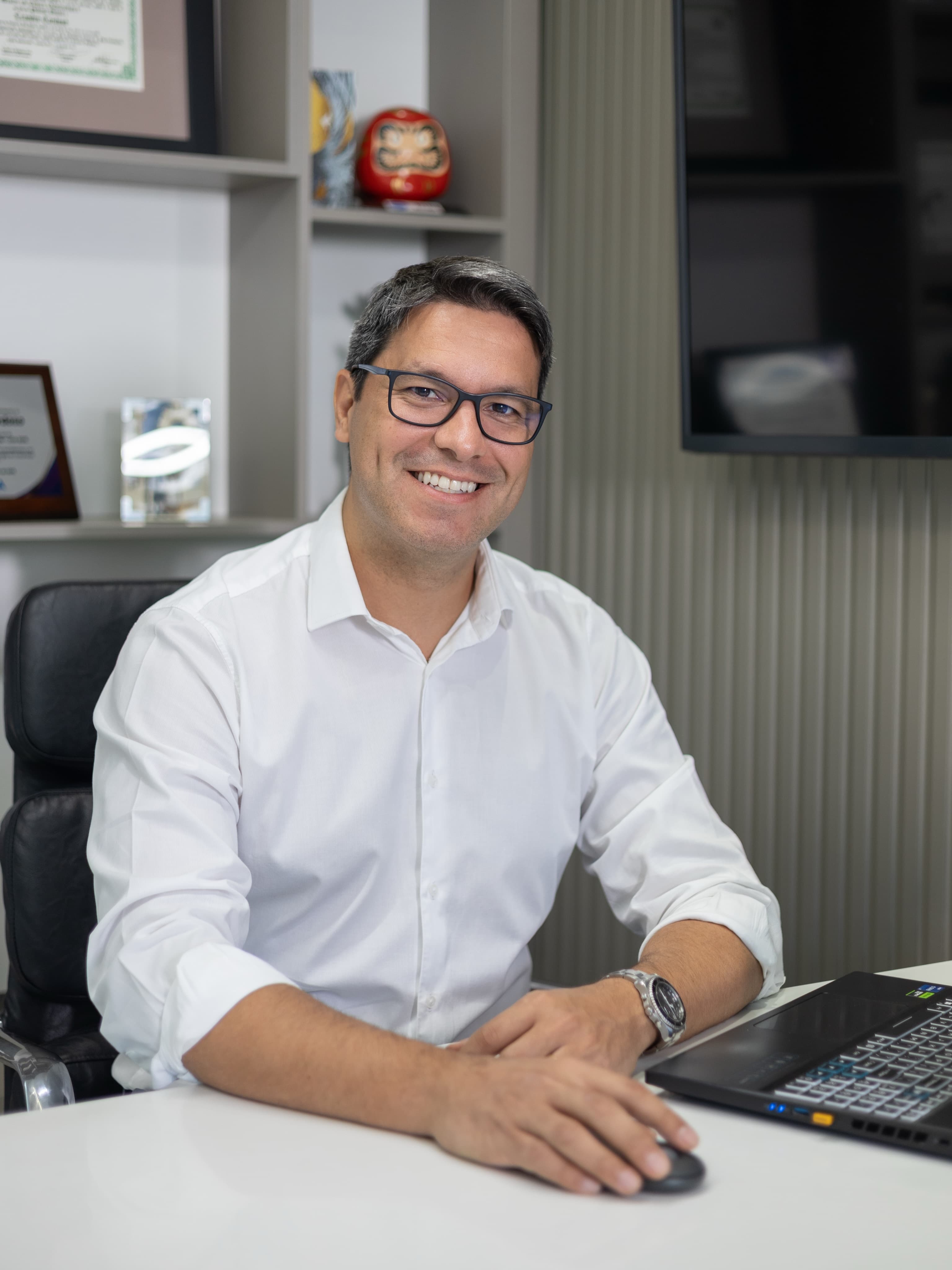Dr. Leandro sorrindo na mesa do consultório, com o notebook aberto
